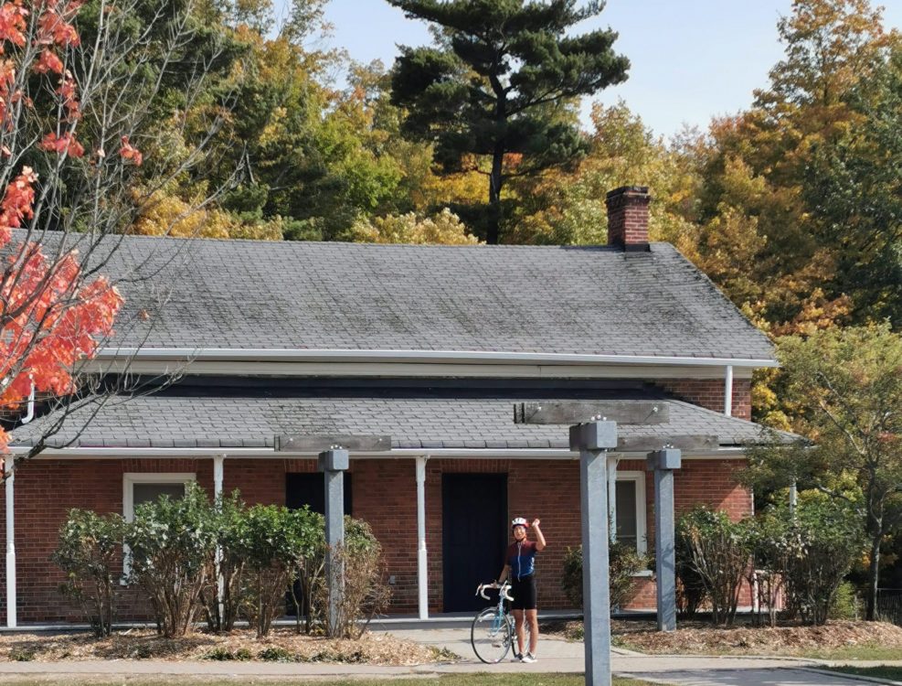 Ride and Seek submission – Baker House Person standing with bicycle in front of historic house