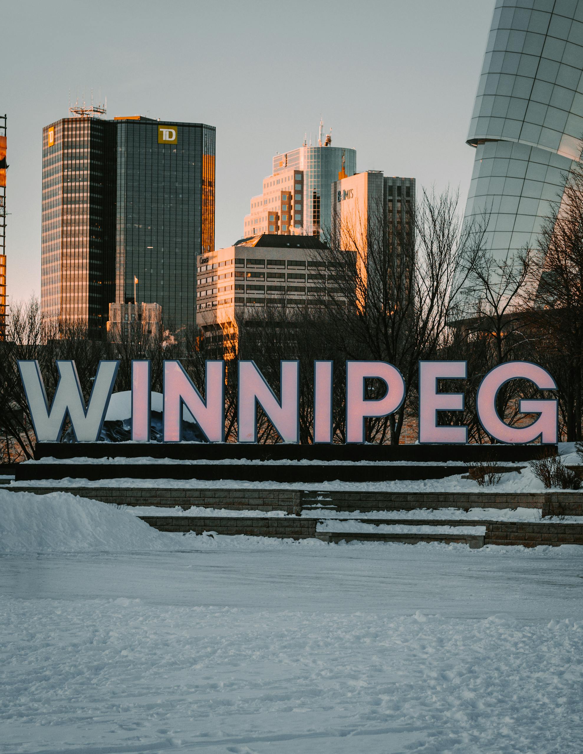A large sign spelling out "WINNIPEG" placed in front of high-rise buildings in the background.